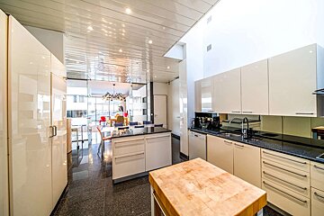 A spacious, modern kitchen featuring cream cabinets, black granite counters, a butcher block island, and a dining area visible through an open archway.