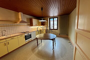 A kitchen featuring pale yellow cabinets, a round wooden dining table, a wooden paneled ceiling, and a window at the back.