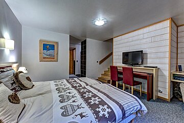 Cozy cabin bedroom featuring winter-themed bedding, a TV desk with red chairs, and stairs in the background.