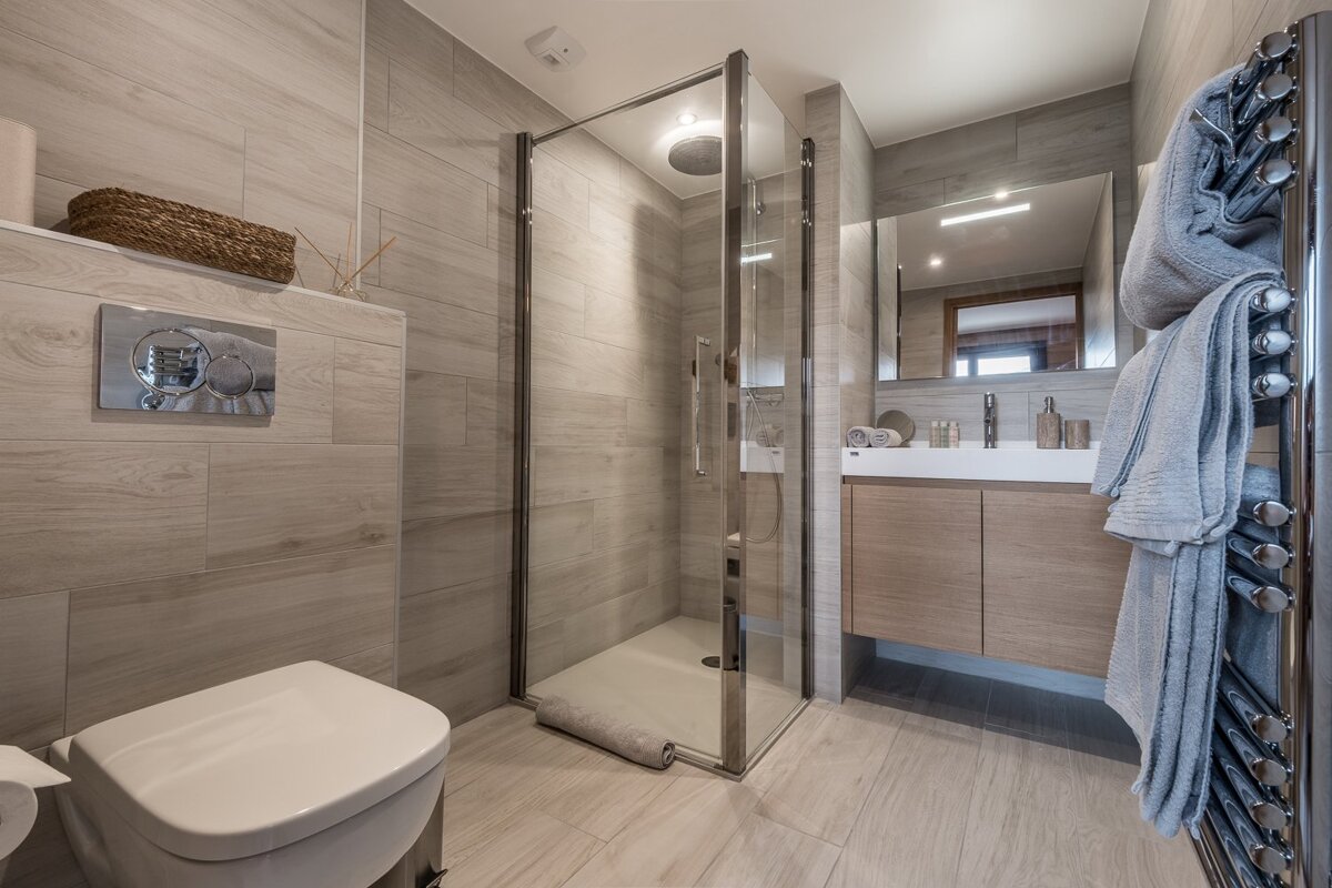 A modern bathroom in neutral tones with a glass shower, toilet, floating vanity, mirror, and a chrome heated towel rail.
