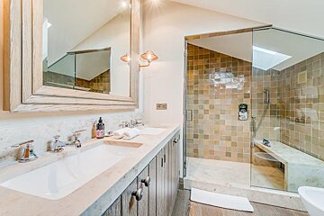 A stylish bathroom featuring a double vanity with a large mirror, and a spacious glass-enclosed shower with earthy-toned tiles and a built-in bench.