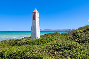 A white obelisk with a red top sits on a hill overlooking the ocean
