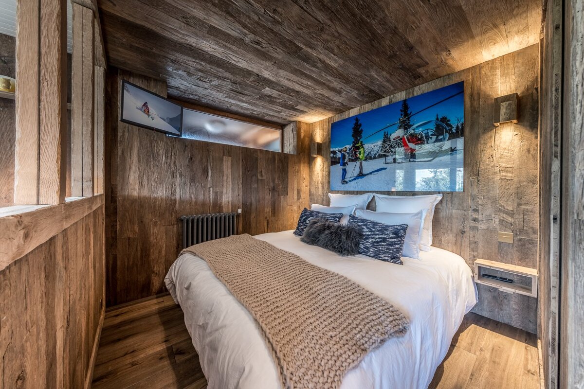 Cozy wood-paneled bedroom with a large bed, ski-themed artwork, and a TV. The rustic decor creates a chalet-like ambiance.