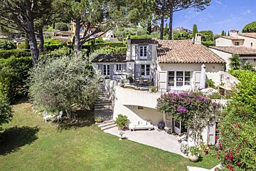A charming multi-level Mediterranean villa on a sunny hillside, featuring terracotta roofs, stone terraces, and lush green gardens.