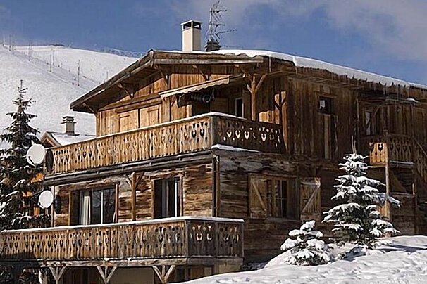 A wooden house with a balcony is covered in snow
