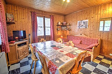 Cozy, wood-paneled room with a dining table, patterned red decor, a sofa, TV, and a distinctive black/white checkered floor.