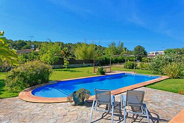 A large swimming pool is surrounded by a stone patio and chairs