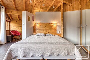 A warm, rustic-modern bedroom with wood-paneled walls and ceiling, a large bed with a wooden headboard, and a bright red chair.