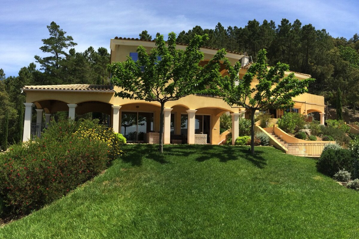 A large house sits on top of a lush green hillside
