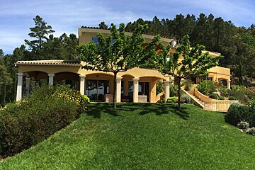 A large house sits on top of a lush green hillside