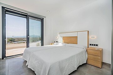 A bright, modern bedroom features two beds pushed together, a wooden headboard, and large sliding glass doors opening to a scenic landscape view.