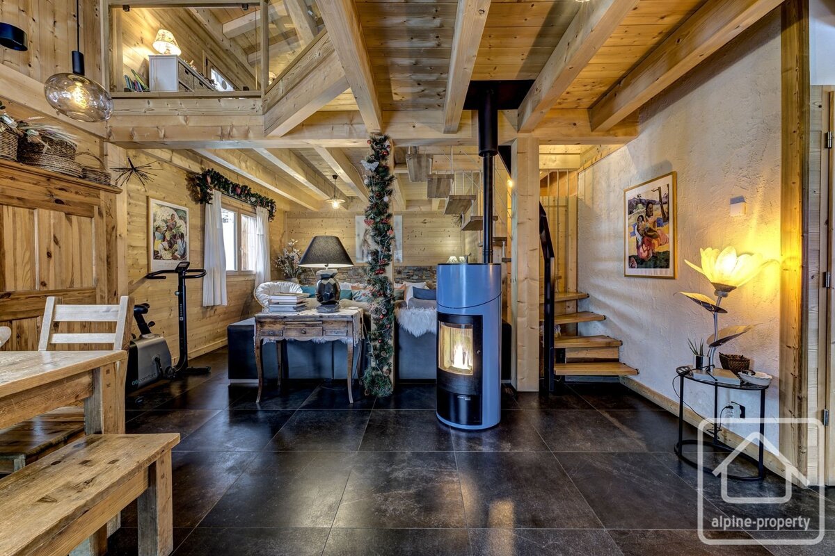 Rustic wooden chalet living room with a modern blue fireplace, dark tiled floor, and wooden beams. A cozy, multi-level space.