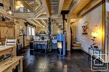Rustic wooden chalet living room with a modern blue fireplace, dark tiled floor, and wooden beams. A cozy, multi-level space.