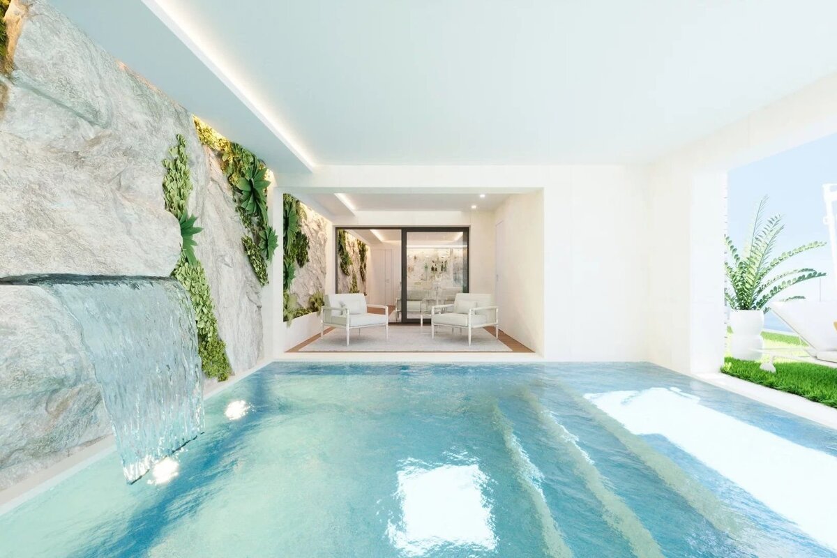 A modern indoor pool with a waterfall from a rock wall adorned with plants, leading to a seating area and an outdoor view.
