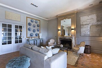 An elegant living room featuring a gray sofa, a classic fireplace with a large mirror, and walls adorned with blue decorative plates.