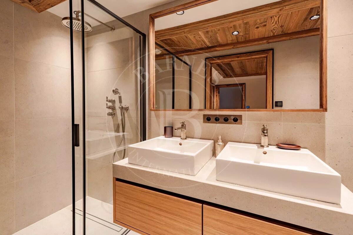 Modern bathroom with double vessel sinks, a wooden vanity, a large wood-framed mirror, and a glass-enclosed shower.