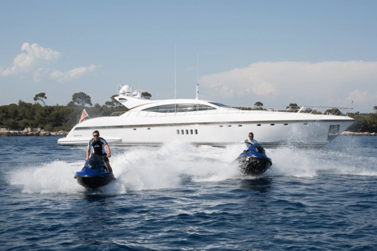 Two people are riding jet skis in front of a large white boat