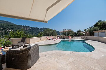 A large swimming pool is surrounded by chairs and an awning