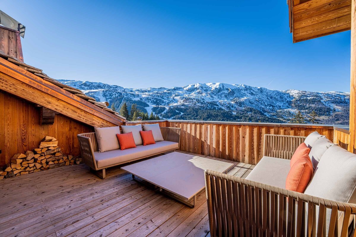 A wooden deck with a couch and a table with mountains in the background