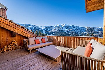 A wooden deck with a couch and a table with mountains in the background