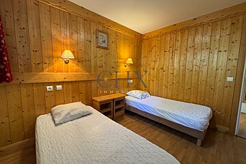 Cozy wood-paneled bedroom featuring two twin beds with white linens, bedside tables, and warm wall lighting in a rustic chalet style.