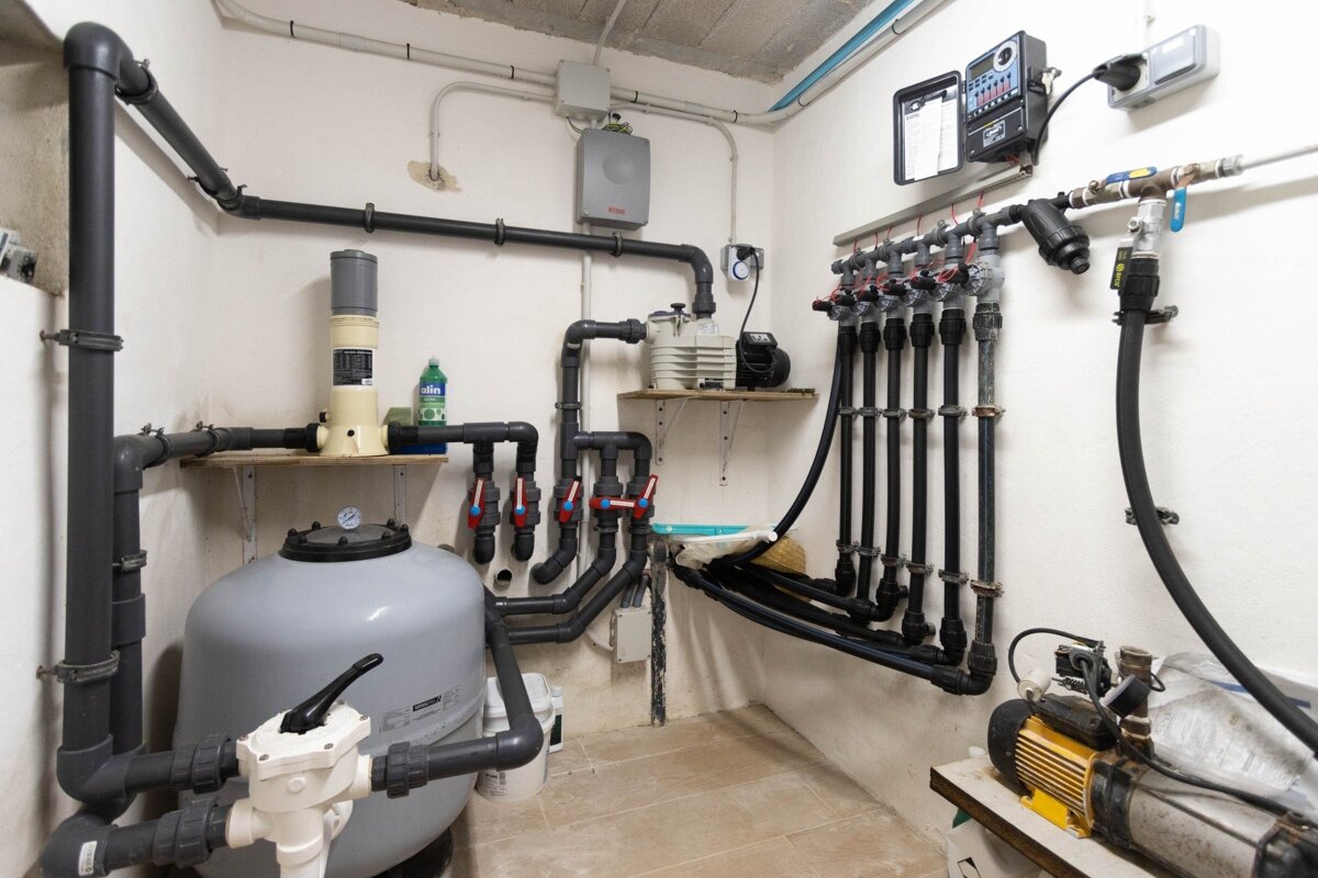 A utility room filled with a complex network of pipes, pumps, filters, and control panels neatly installed against white walls.