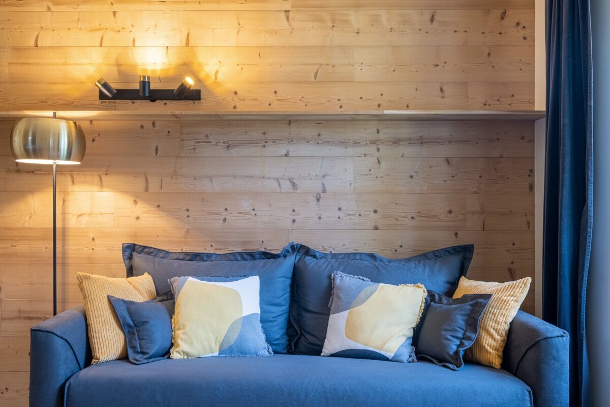 A blue couch with yellow pillows sits in front of a wooden wall