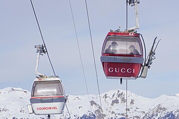 A red Gucci cable car and a white Courchevel cable car suspended high above snowy mountain peaks.