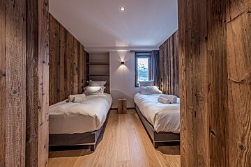 A cozy wooden cabin bedroom with two twin beds made in white linens, framed by rustic timber walls.