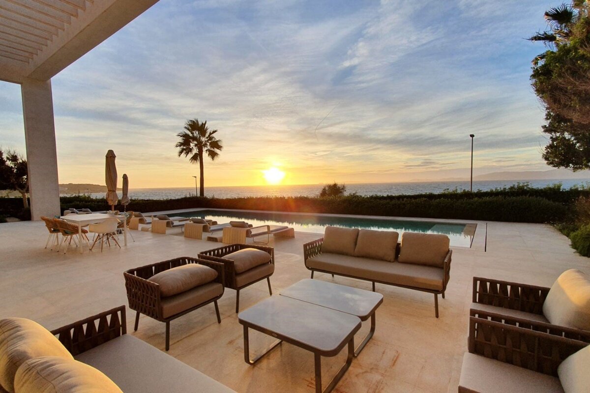 The sun is setting over the ocean behind a couch and chairs