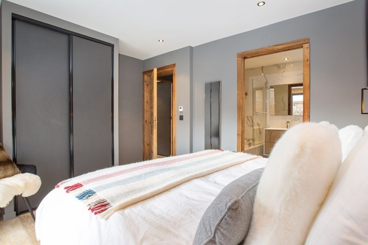 Modern grey bedroom with a bed in the foreground, sliding closet doors, and a doorway leading into an ensuite bathroom.