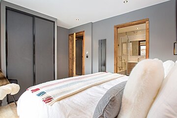 Modern grey bedroom with a bed in the foreground, sliding closet doors, and a doorway leading into an ensuite bathroom.