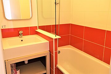 A bright bathroom with red and white tiled walls, a white sink under a mirror, and a bathtub with a glass shower screen.