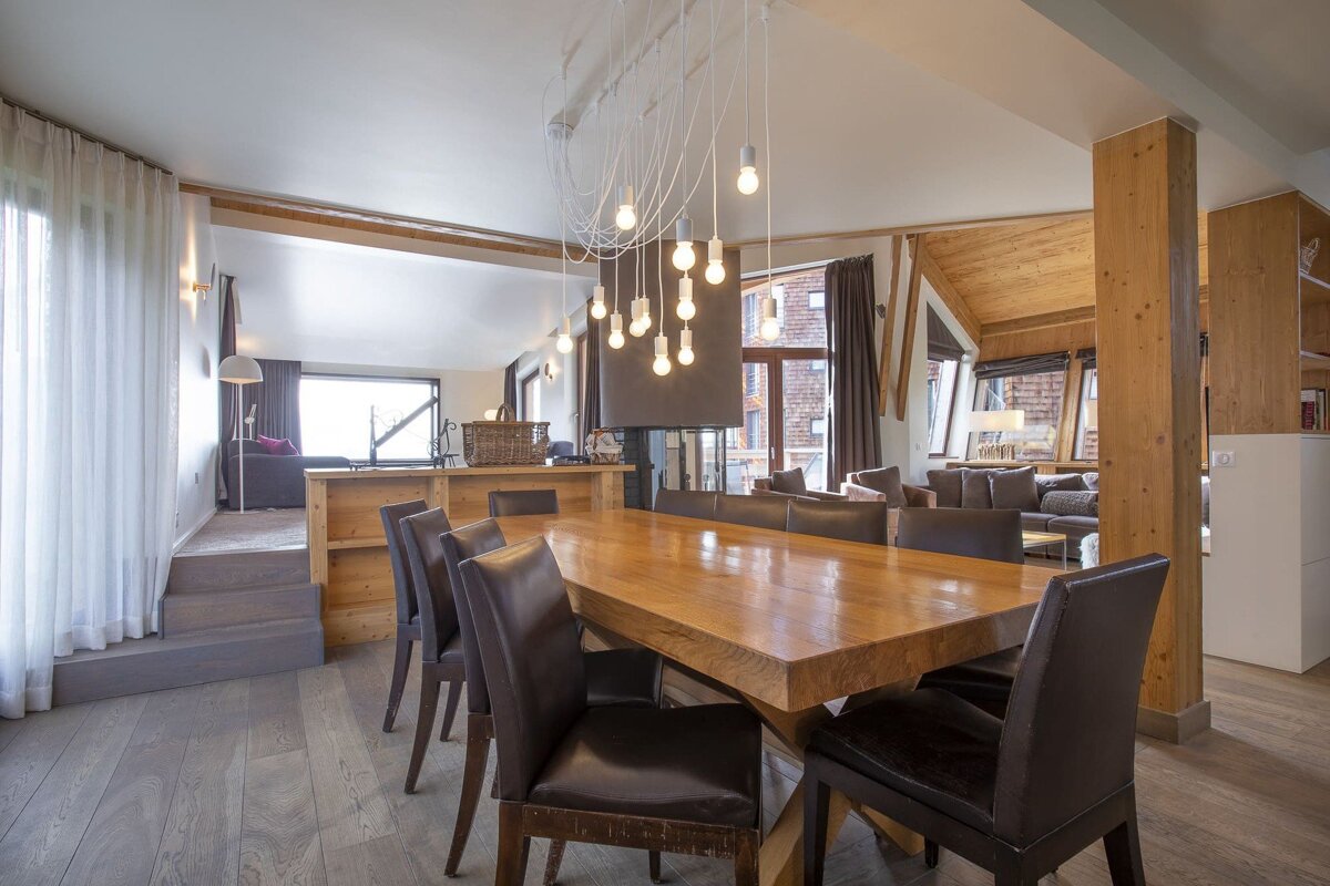 Modern rustic dining area with a long wooden table, dark leather chairs, and a creative hanging bulb light fixture.