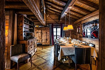 Cozy, rustic dining room in a wooden chalet with exposed beams, a set dining table, and modern pendant lights.