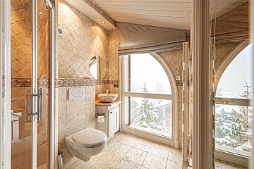 Cozy tiled bathroom featuring a modern toilet, stone sink, and a large arched window with views of a snowy winter landscape.