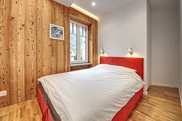 A bedroom with wood paneling and a red bed