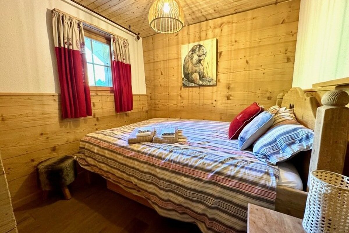 Cozy cabin-style bedroom featuring wood-paneled walls, a striped bed, red curtains, and a marmot painting.