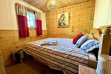 Cozy cabin-style bedroom featuring wood-paneled walls, a striped bed, red curtains, and a marmot painting.