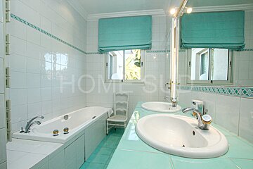 A bathroom with two sinks and a tub has the word home on the wall