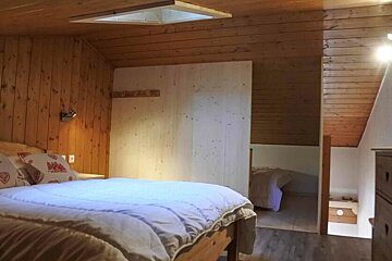 A cozy, wood-paneled cabin bedroom with a bed in the foreground, a skylight, and another sleeping area visible in the background.