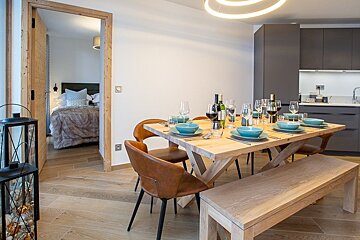 A set wooden dining table in a modern apartment with a view into a cozy adjacent bedroom.