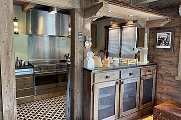 A rustic kitchen with wood beams/paneling, a large stainless steel range, geometric tiled floor, and a counter with a coffee maker.