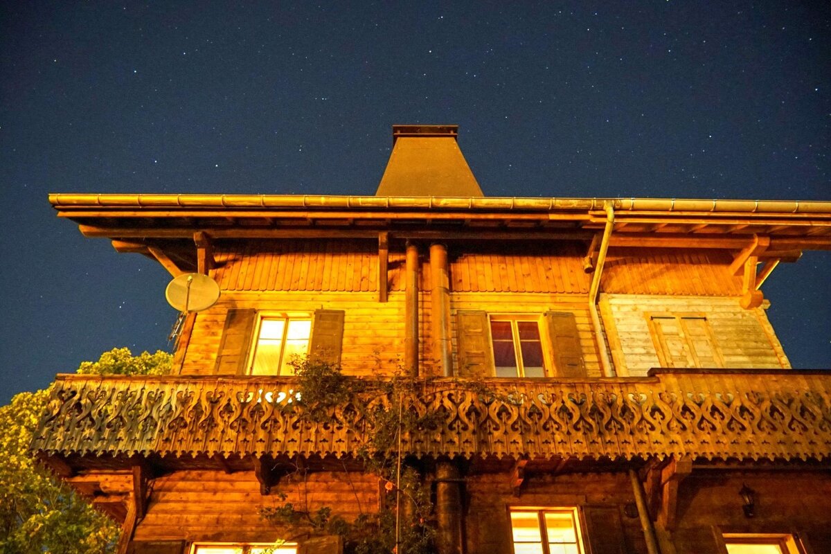 A warmly lit wooden chalet with an ornate balcony under a starry night sky.