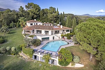 An aerial shot of a luxury villa with a swimming pool and lush green lawn in France, surrounded by trees.