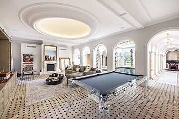 Luxurious game room with a clear pool table, patterned tile floor, fireplace, pinball machine, and arches leading to an indoor pool.