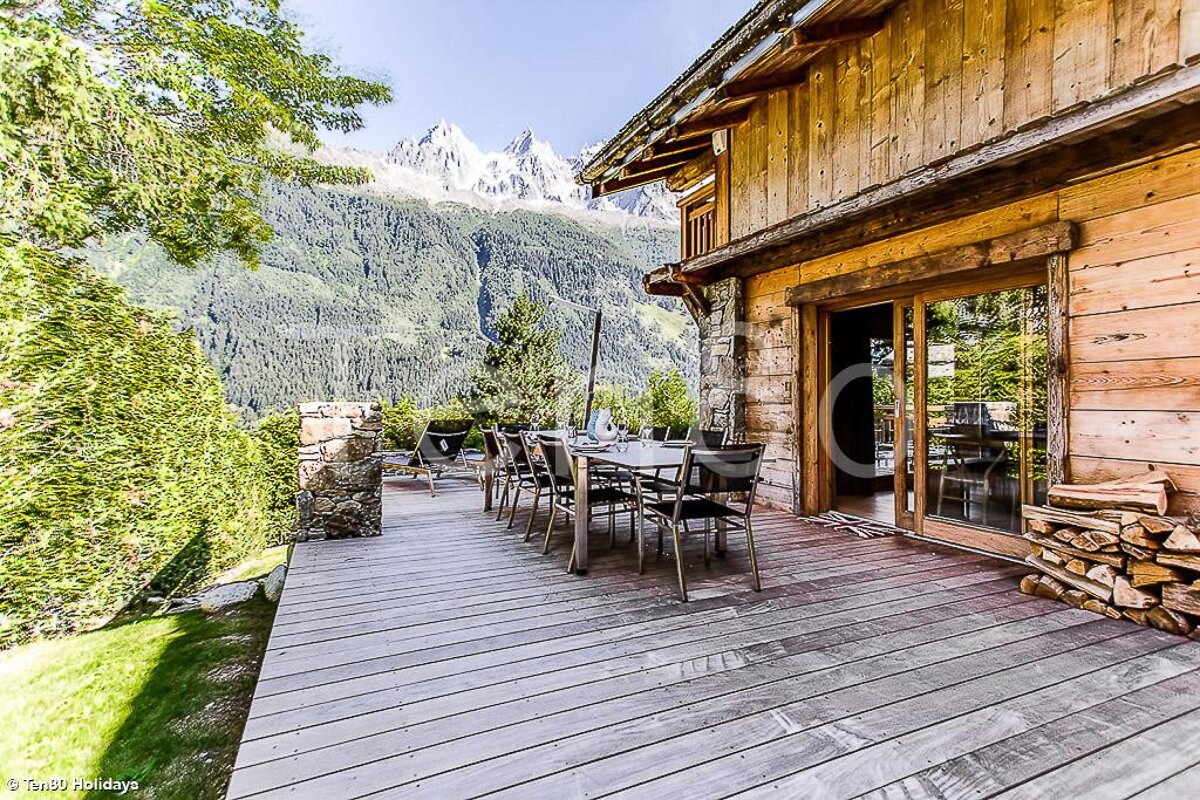 A wooden deck with a table and chairs and mountains in the background