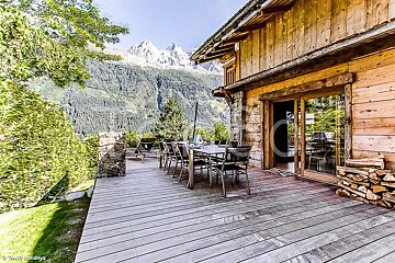 A wooden deck with a table and chairs and mountains in the background