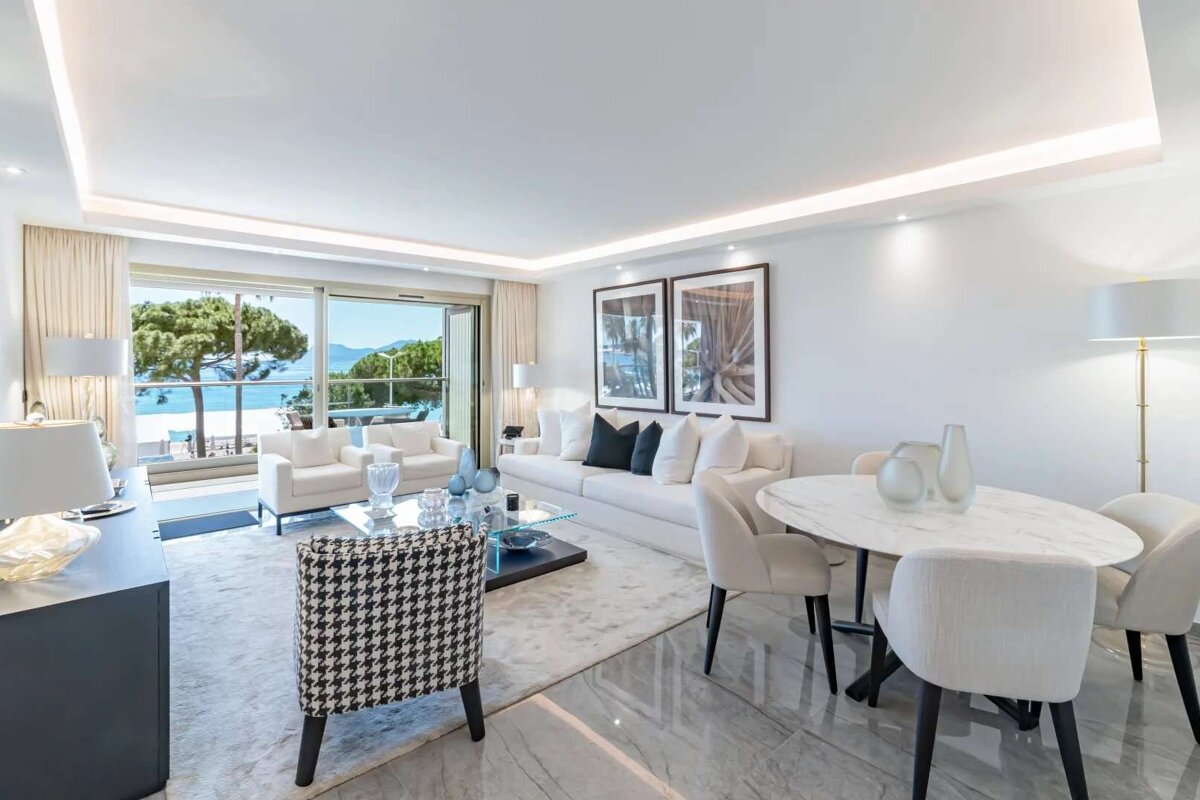 A luxurious, modern living and dining room with white furniture, a houndstooth chair, and a stunning sea view through an open balcony.