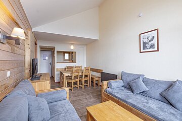 A rustic yet modern living and dining area with wood accents, gray sofas, a wooden table, and a mountain print.